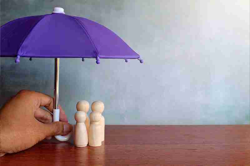 Hand holding purple umbrella over wooden family figures on table, symbolising insurance protection for Australian families.