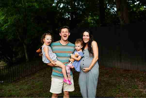 Joyful young family outdoors with father excitedly holding two toddlers and pregnant mother smiling, symbolizing family security through life insurance in Australia.